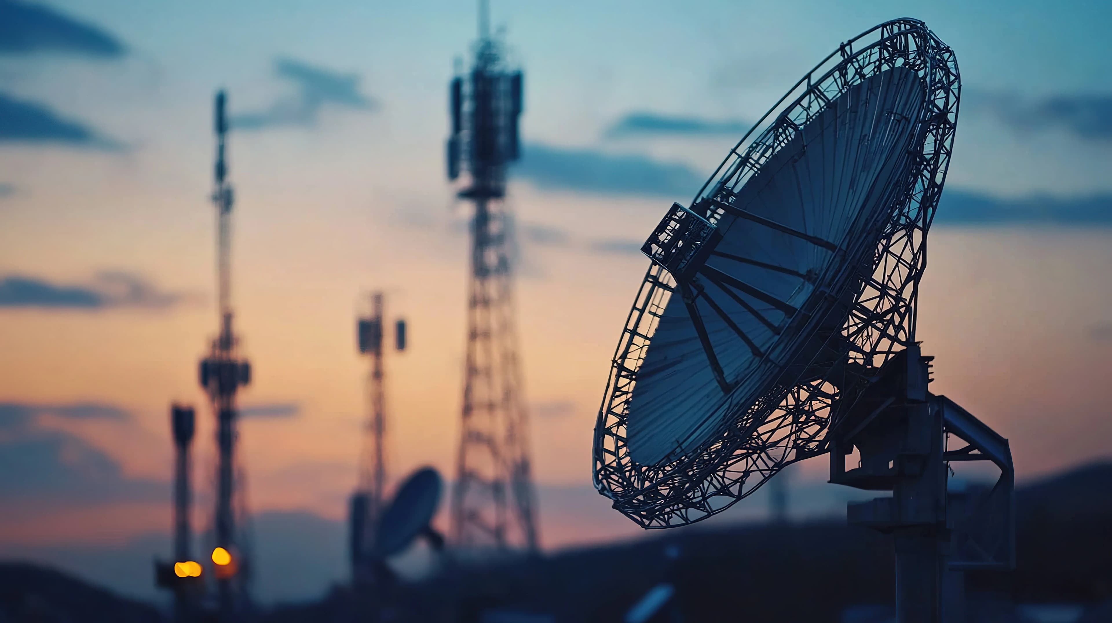 Large satellite dish with telecommunication towers and a sunset