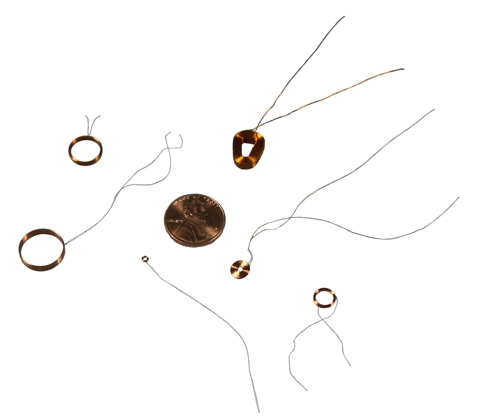Six various size miniature self-supporting coils next to a penny for size reference